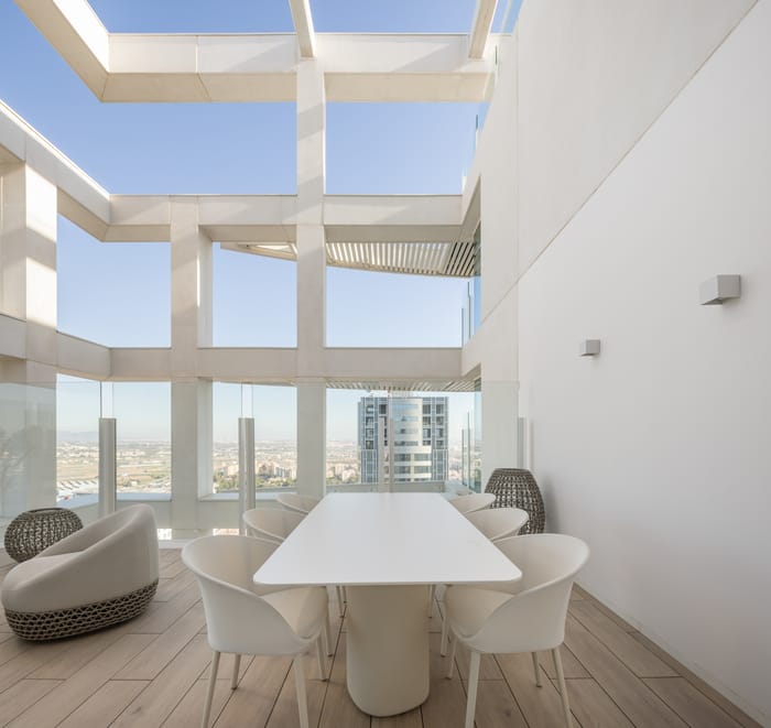 Espacio exterior en la Torre IKON, Valencia, decorado con plantas en macetas de cerámica artesanal, mesa de comedor al aire libre y sillones de ratán natural