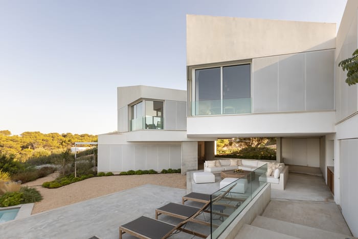 Fachada de una casa en Menorca de estilo mediterráneo minimalista, con paredes encaladas, detalles de madera natural y jardines que reflejan el paisaje local