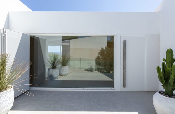 Fachada principal en una casa mediterránea de Menorca, con arcos en los porches, acabados en yeso natural y maceteros de cerámica tradicional.