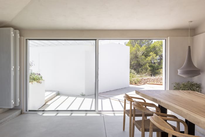 Interior de estilo mediterráneo minimalista en Menorca, con paredes blancas, mobiliario de líneas simples y grandes ventanales que integran el paisaje exterior