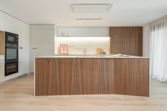 Cocina contemporánea con una isla central personalizable, acabados en madera natural y encimeras de porcelánico de alta resistencia.