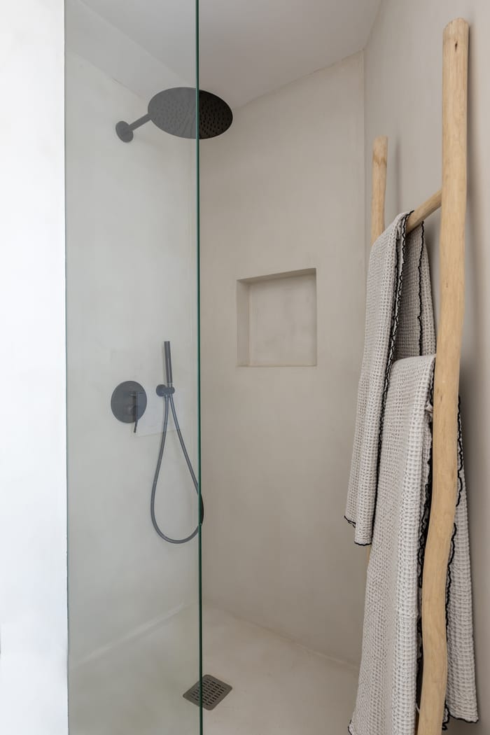 Espacio de baño relajante en Menorca, con materiales sostenibles: lavamanos de piedra volcánica, estanterías de madera reciclada y toalleros calefactables