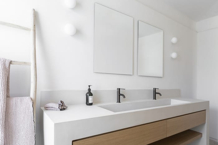 Baño principal en una casa de Menorca, con diseño minimalista mediterráneo: lavabo de piedra natural, ducha de microcemento y grifería negra mate