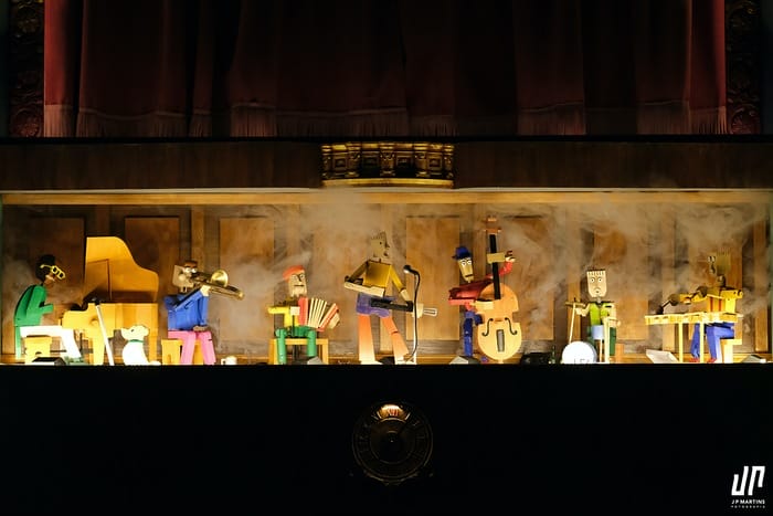 Escenografía minimalista con títeres y juego de luces suaves.