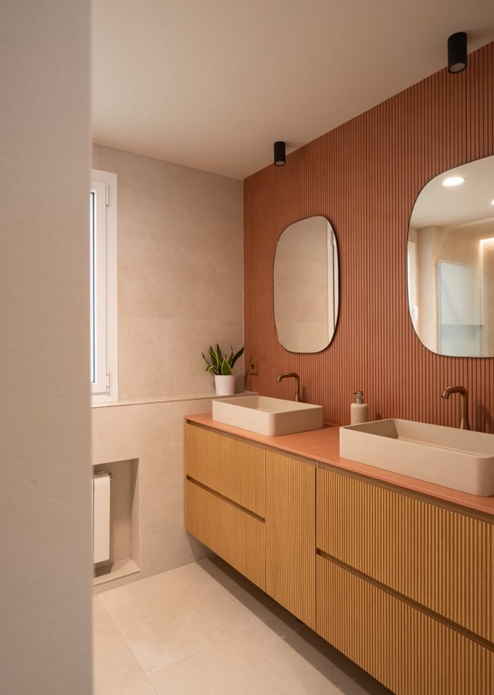 año contemporáneo con doble lavabo, espejo orgánico y revestimiento en tonos terracota.