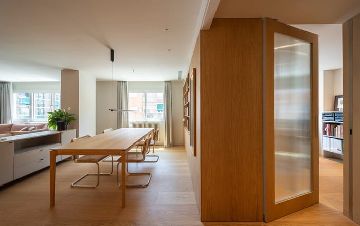 Vista del comedor con mesa de madera, sillas de rejilla y estanterías empotradas junto a gran ventanal.