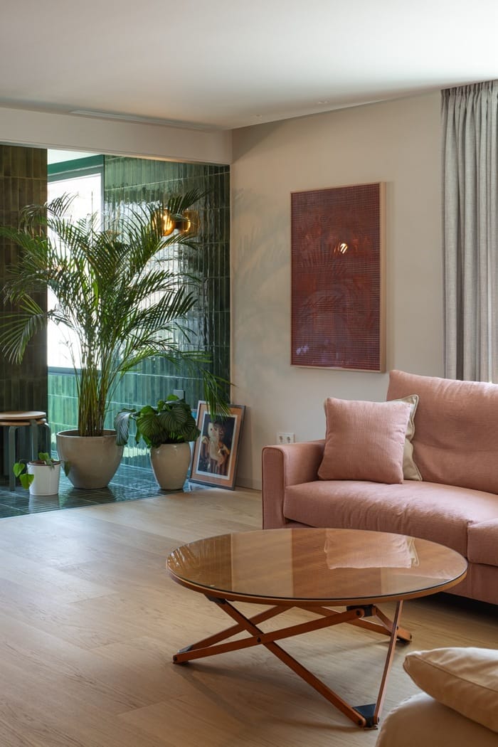 Detalle de sofá rosa, mesa baja redonda y plantas junto a la zona acristalada de la terraza interior