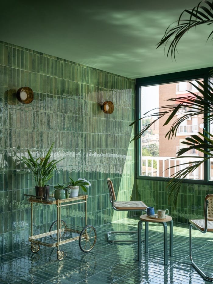 Zona de descanso interior con sillas de enea y carrito auxiliar sobre pavimento verde esmaltado.