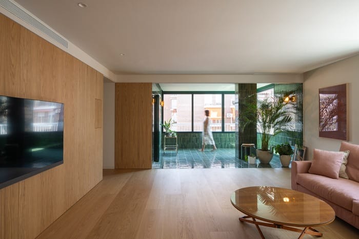 Salón con sofá rosa empolvado y conexión directa a la terraza interior revestida con cerámica verde.