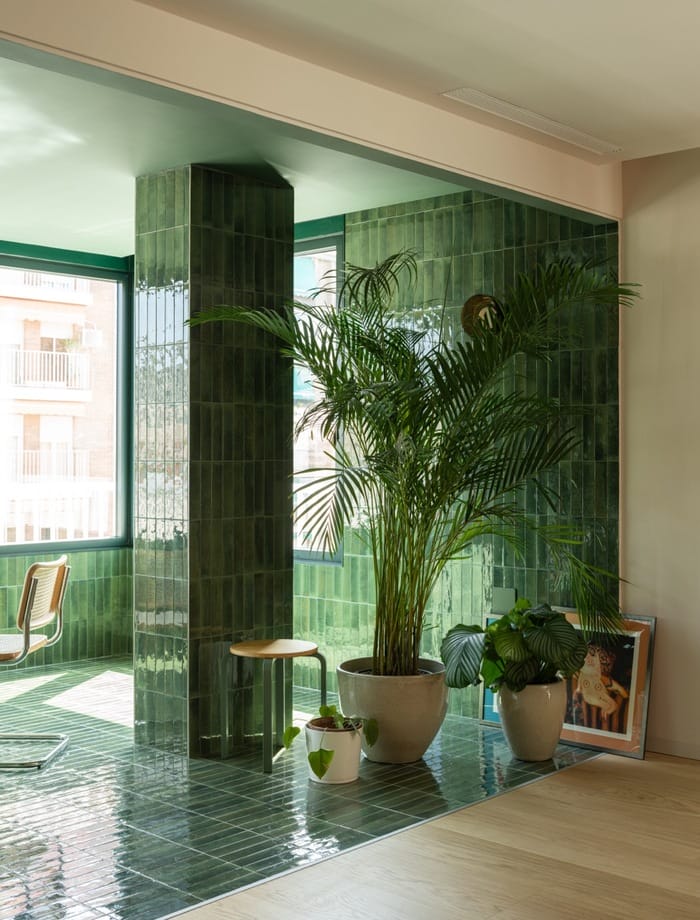 Terraza interior revestida en cerámica verde brillante con grandes macetas y luz natural.