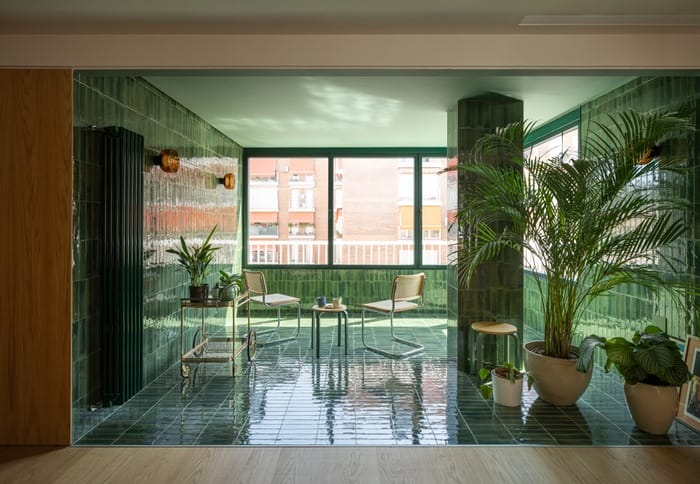 Terraza interior con azulejos verdes esmaltados, plantas naturales y mobiliario ligero de diseño.