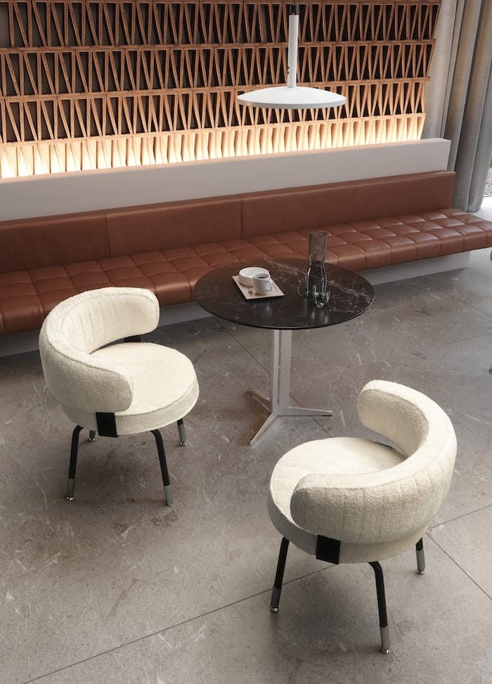 Par de sillas blancas de diseño curvo alrededor de una mesa circular de mármol, en un ambiente de hostelería con banco de piel marrón y pared decorativa retroiluminada.